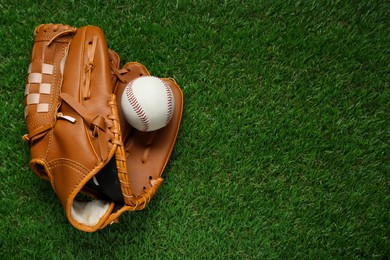Photo of Catcher's mitt and baseball ball on green grass, top view with space for text. Sports game