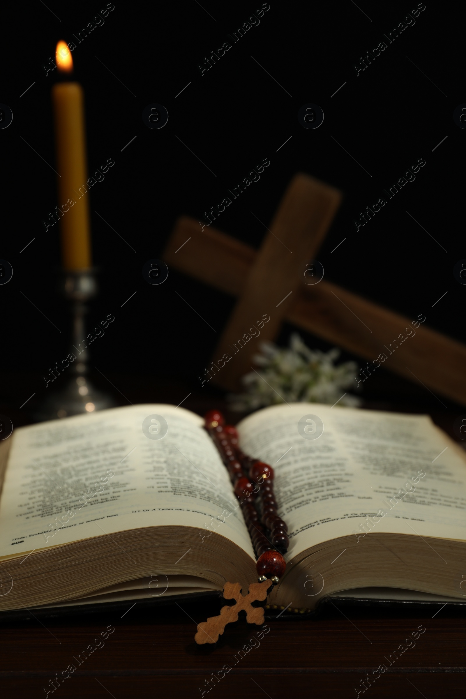 Photo of Crosses, rosary beads, Bible and church candle on wooden table