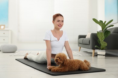 Photo of Happy young woman practicing yoga on mat with her cute dog at home