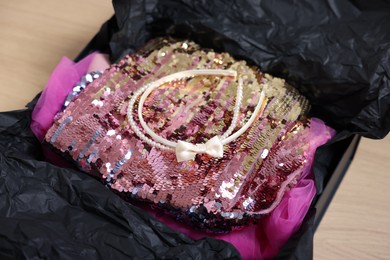 Photo of Headbands and stylish pink carnival costume with sequins in black box on wooden table, closeup