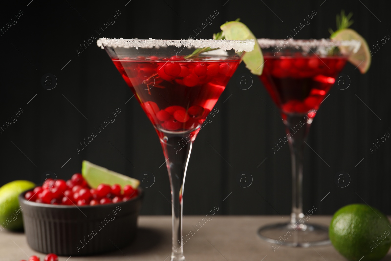 Photo of Tasty cranberry cocktail with rosemary and lime in glasses on grey table against black background, closeup