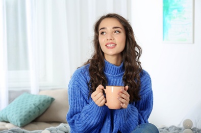 Photo of Young beautiful woman in warm sweater with cup of hot drink at home