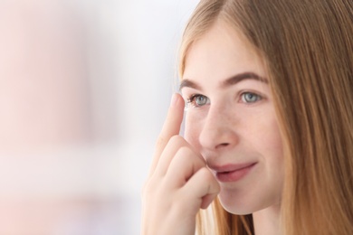 Photo of Teenage girl putting contact lens in her eye on blurred background