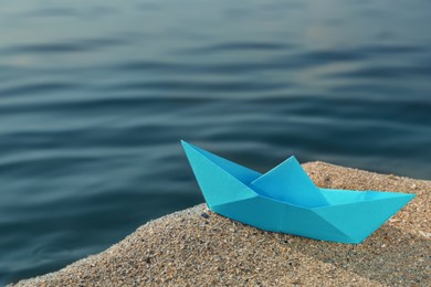 Photo of Light blue paper boat near river on sunny day, space for text