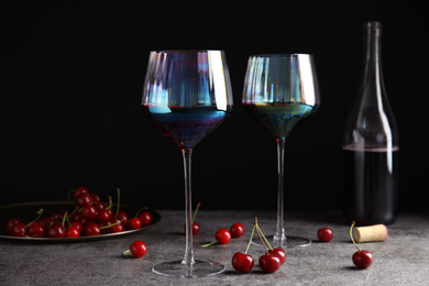 Delicious cherry wine with ripe juicy berries on grey table against black background