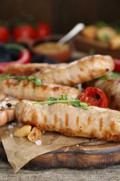 Tasty fresh grilled sausages with vegetables on wooden table, closeup