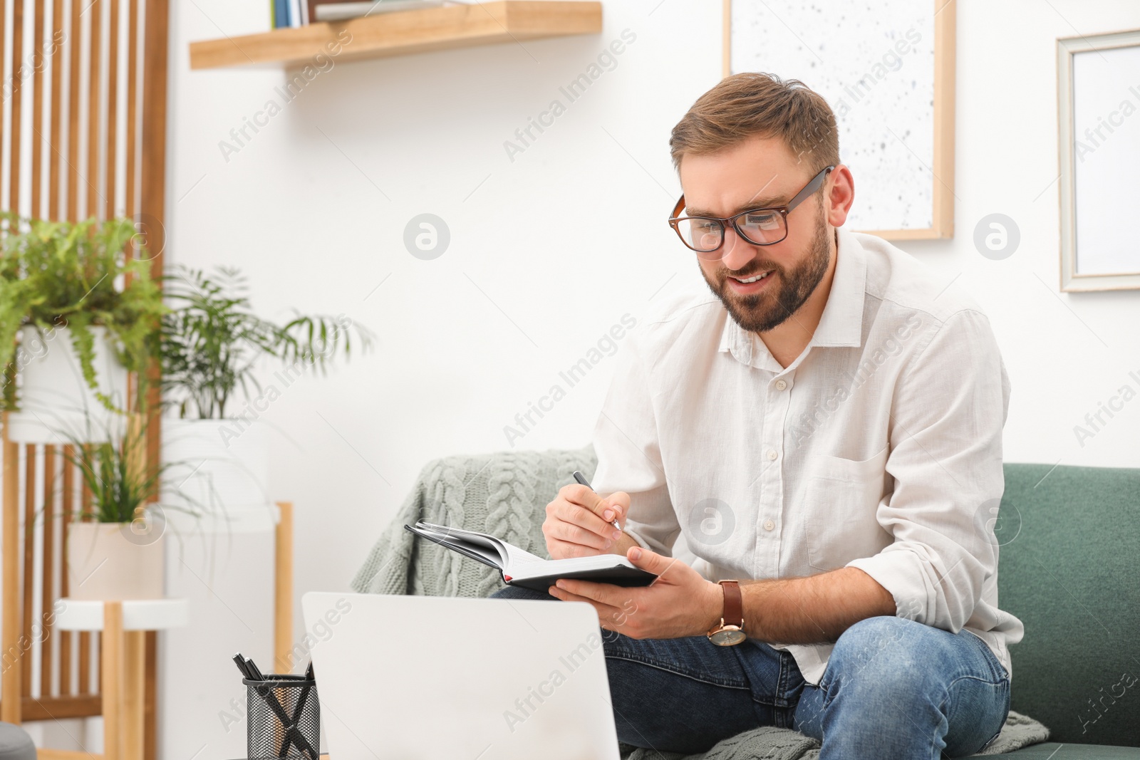 Photo of Young man working with notebook and laptop at home, space for text