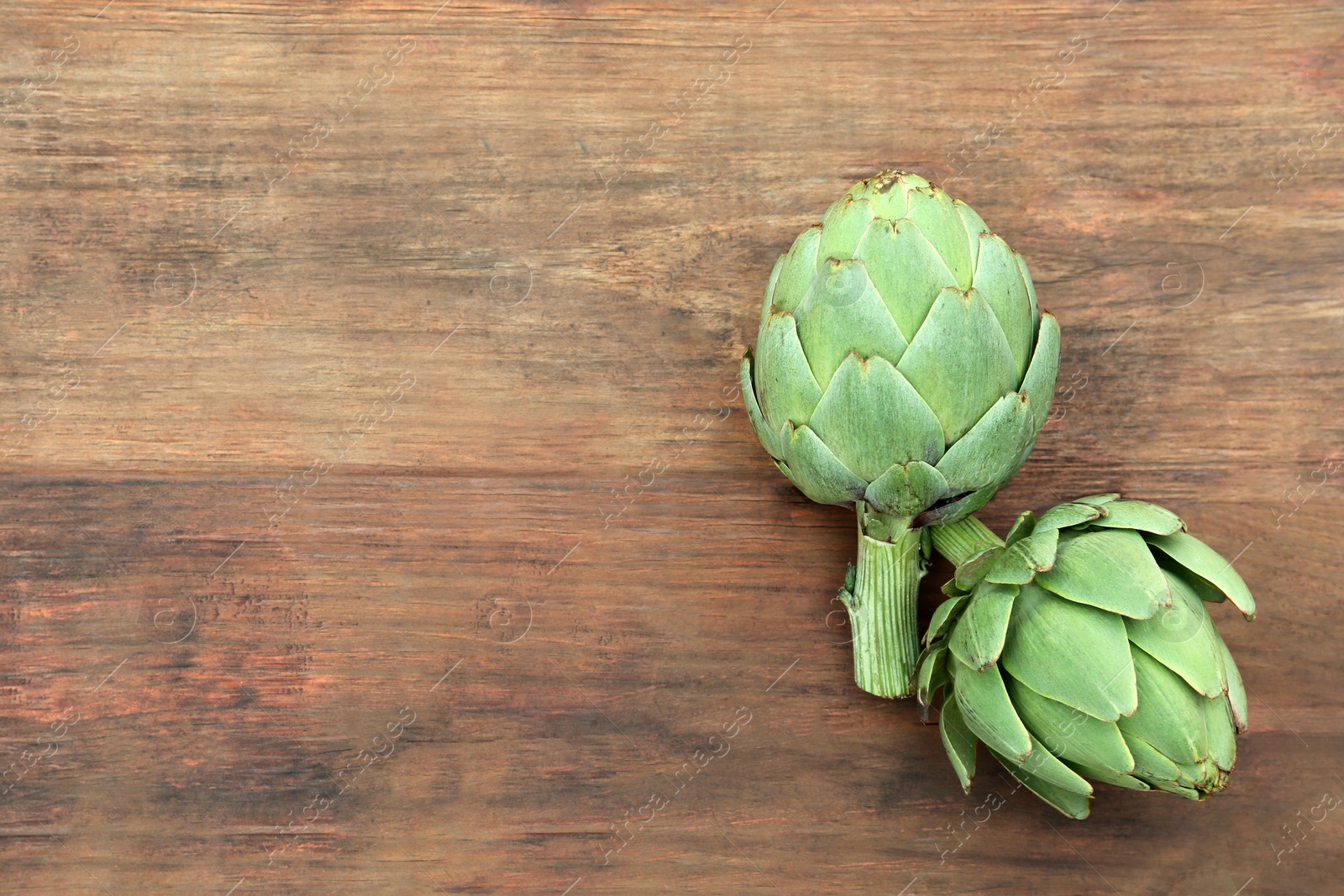 Photo of Fresh raw artichokes on wooden table, flat lay. Space for text