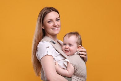 Mother holding her child in sling (baby carrier) on orange background