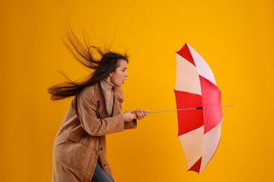 Emotional woman with umbrella caught in gust of wind on yellow background