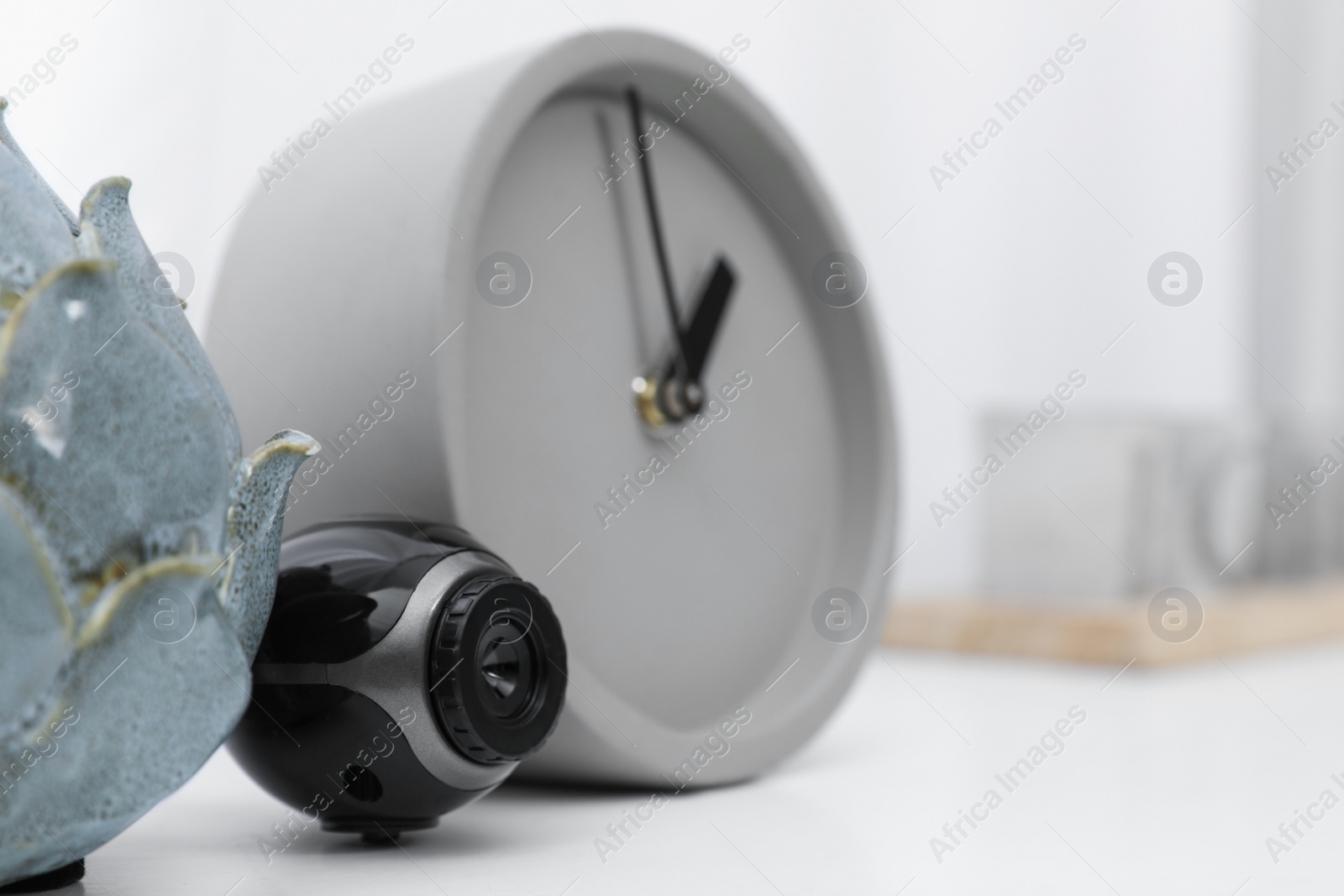 Photo of Small camera hidden near alarm clock on white table indoors, closeup