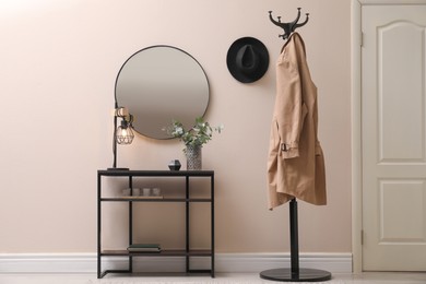 Console table, clothes rack and mirror on beige wall in hallway. Interior design