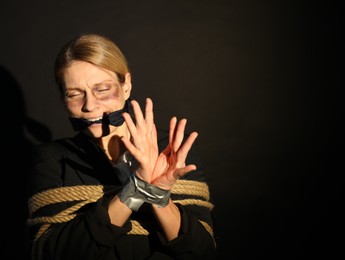 Woman with bruises tied up and taken hostage on dark background