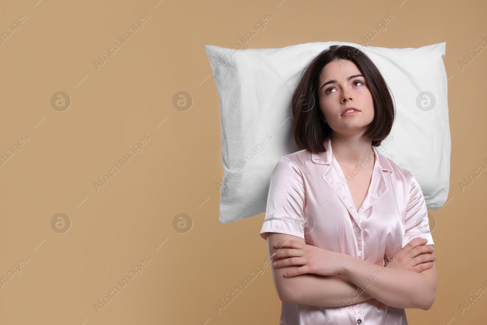 Photo of Unhappy young woman with pillow on beige background, space for text. Insomnia problem