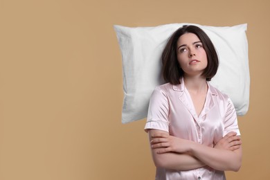 Photo of Unhappy young woman with pillow on beige background, space for text. Insomnia problem