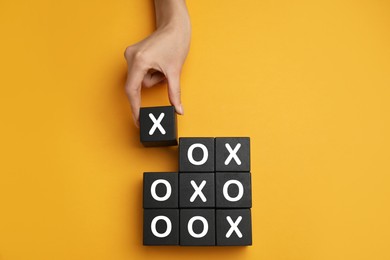 Photo of Woman playing tic tac toe game on yellow background, top view