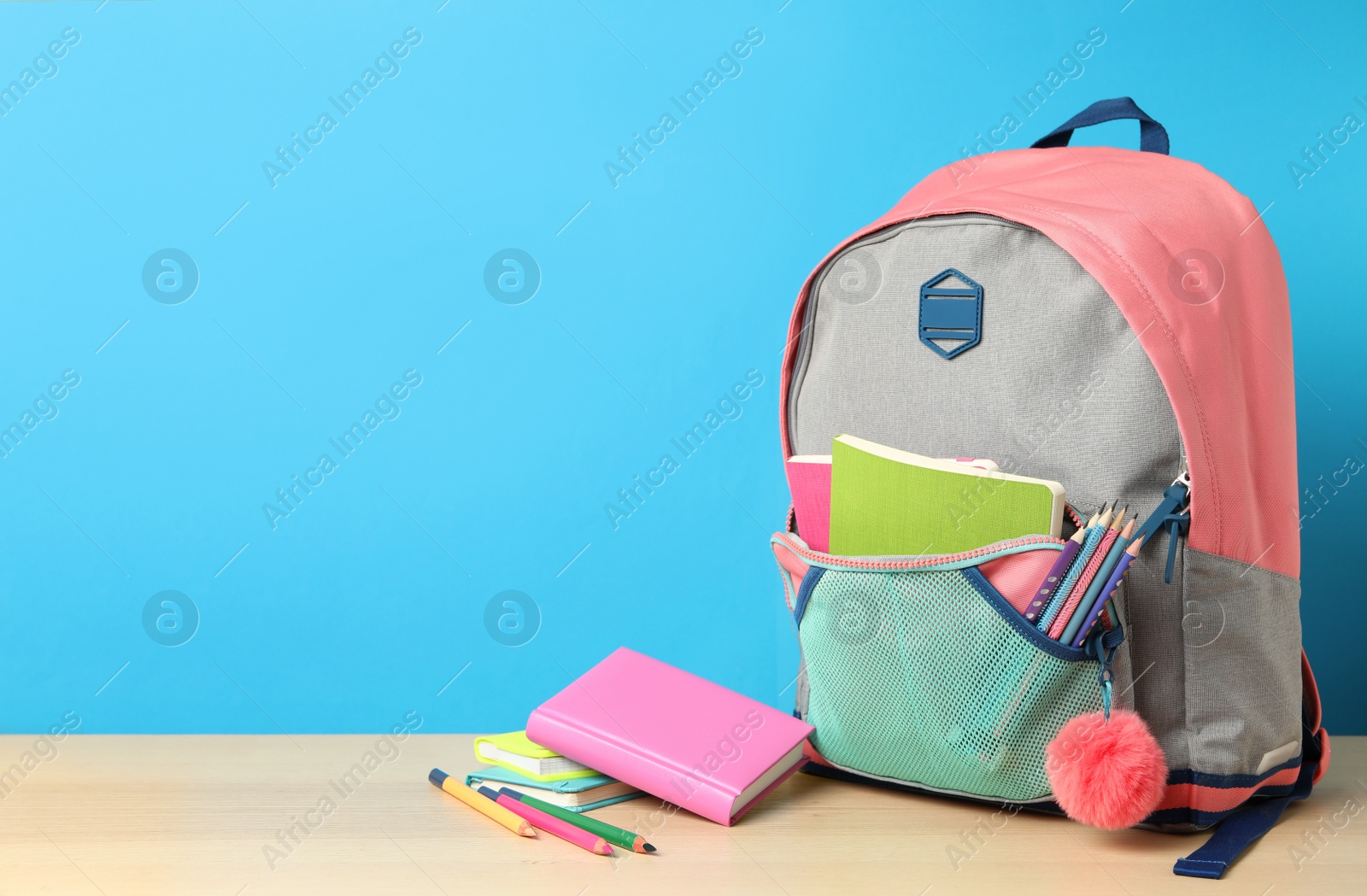 Photo of Stylish backpack and different school stationery on wooden table against light blue background, space for text. Back to school