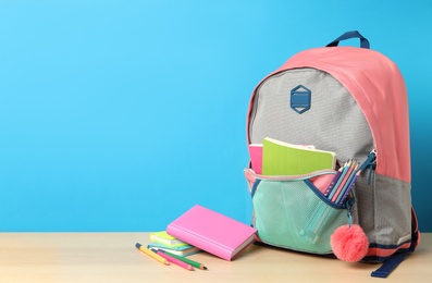 Photo of Stylish backpack and different school stationery on wooden table against light blue background, space for text. Back to school