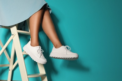 Photo of Woman in stylish sneakers on ladder near color wall, closeup. Space for text