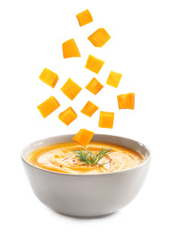 Image of Many pumpkin pieces falling into bowl of homemade soup on white background 