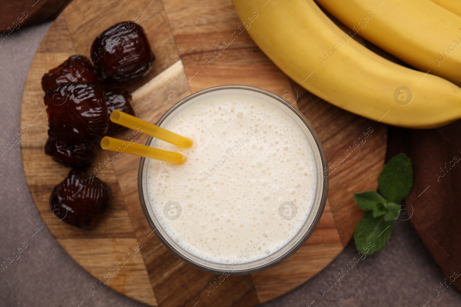 Photo of Glass of delicious date smoothie, dried fruits, mint and bananas on brown table, flat lay