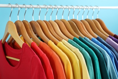 Photo of Rack with bright clothes on blue background. Rainbow colors