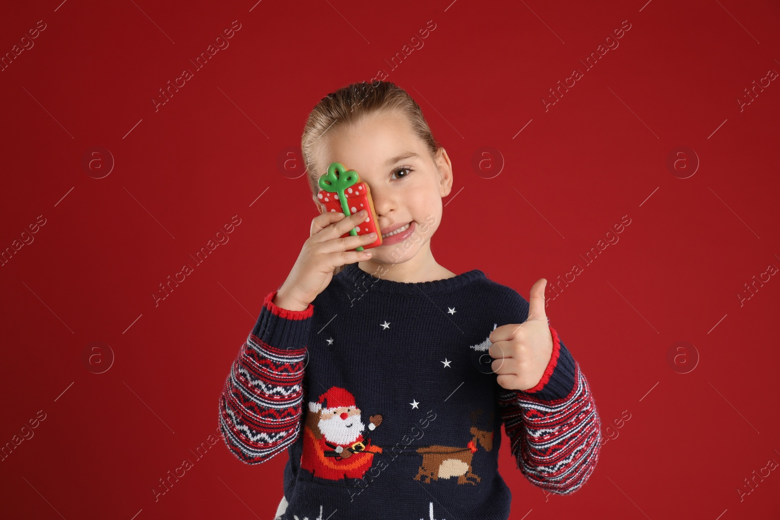 Photo of Cute little girl with Christmas gingerbread cookie on red background