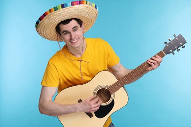 Photo of Young man in Mexican sombrero hat playing guitar on light blue background