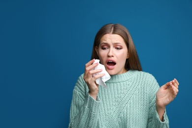 Image of Young woman sneezing on blue background, space for text. Cold symptoms