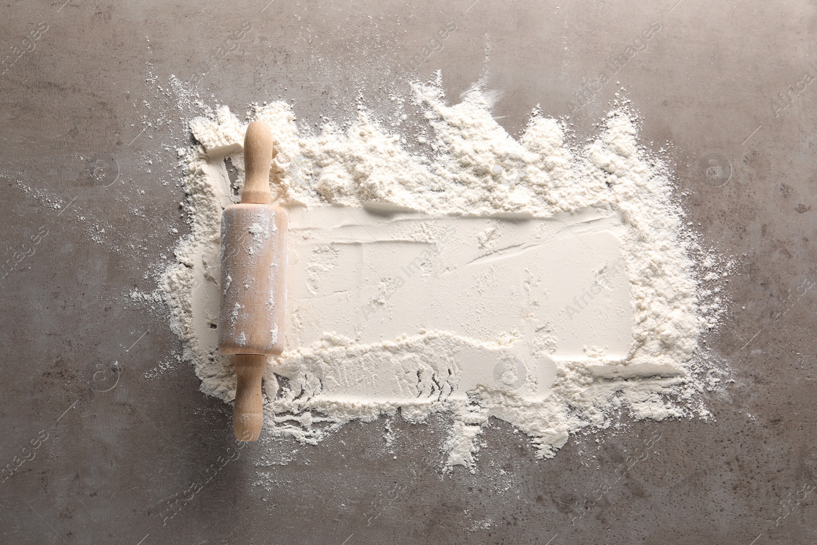 Photo of Scattered flour and rolling pin on grey textured table, top view