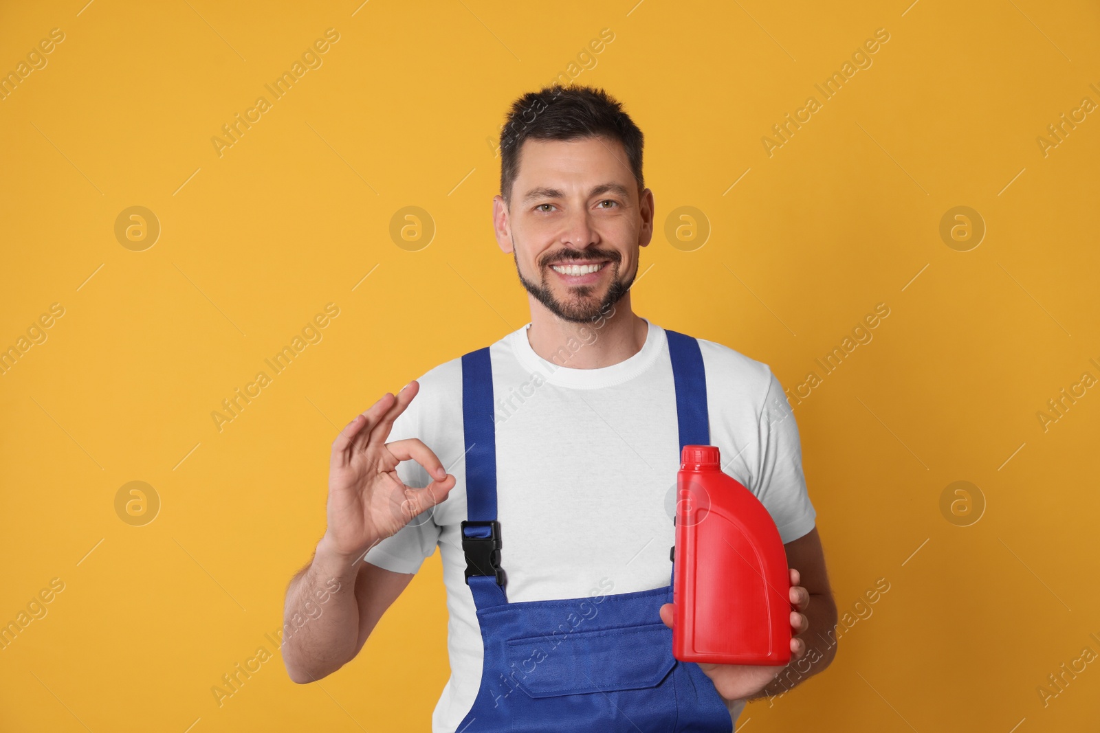 Photo of Man holding red container of motor oil and showing OK gesture on orange background