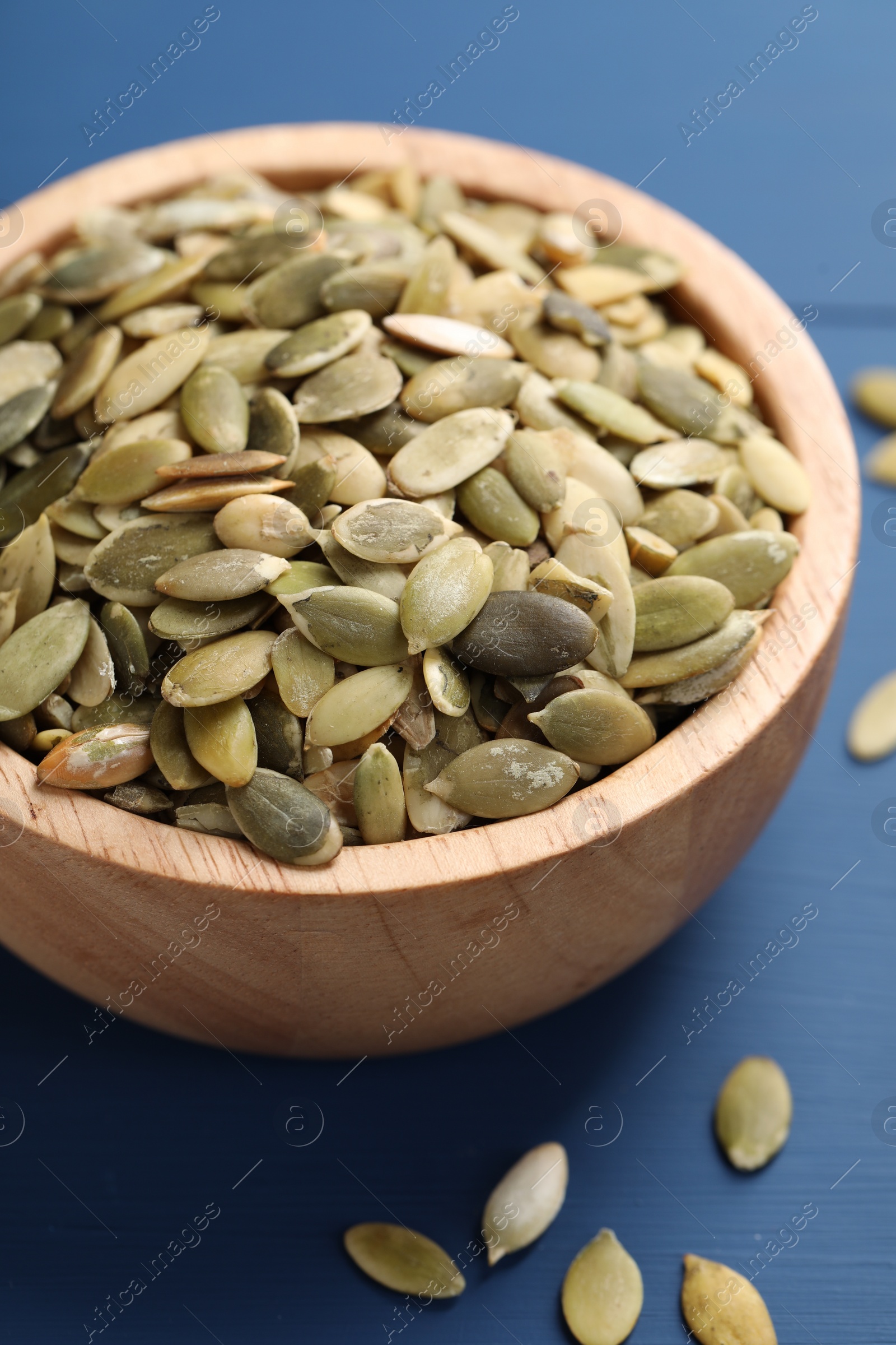 Photo of Bowl with peeled pumpkin seeds on blue wooden table, closeup