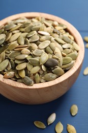 Bowl with peeled pumpkin seeds on blue wooden table, closeup