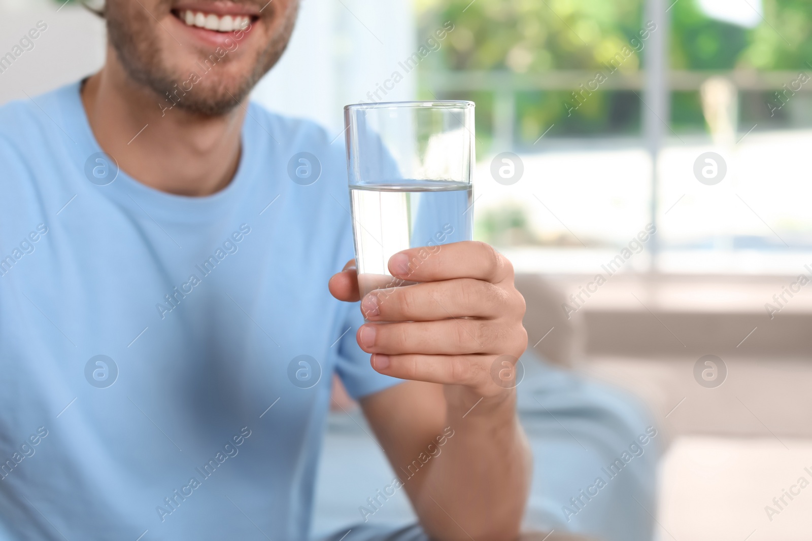 Photo of Young man holding glass of clean water indoors, closeup