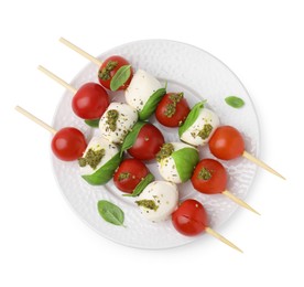 Photo of Plate of Caprese skewers with tomatoes, mozzarella balls, basil and pesto sauce isolated on white, top view