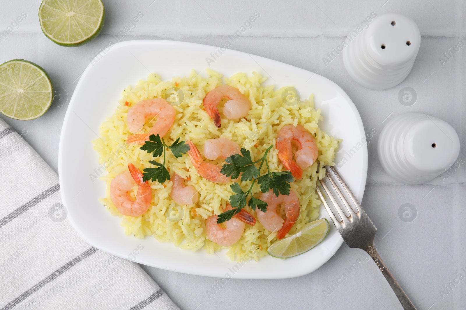 Photo of Delicious risotto with shrimps, lime and parsley on white tiled table, flat lay