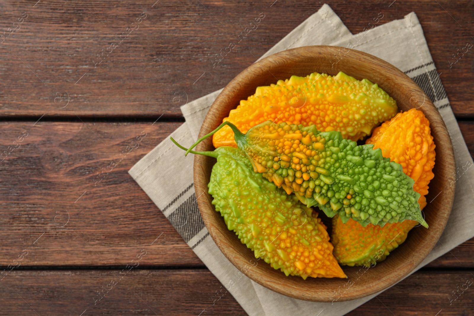 Photo of Bowl with fresh bitter melons on wooden table, top view. Space for text