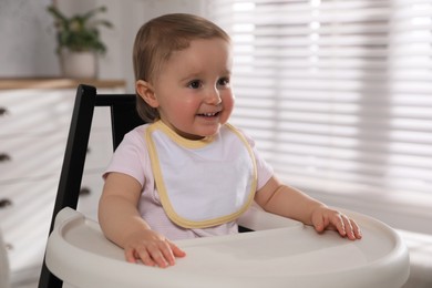 Photo of Cute little baby wearing bib in highchair at home