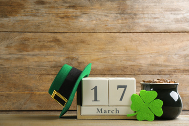 Photo of Composition with pot of gold coins and block calendar on wooden table. St. Patrick's Day celebration