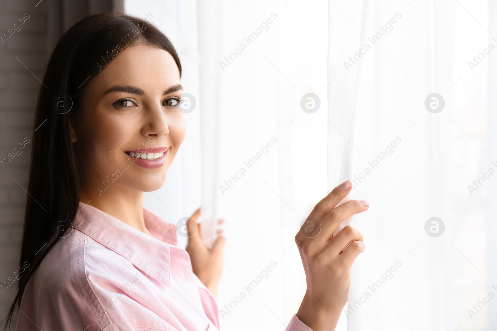 Photo of Woman opening window curtains at home in morning