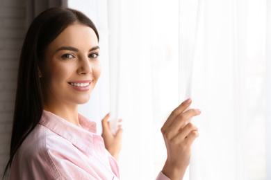 Woman opening window curtains at home in morning