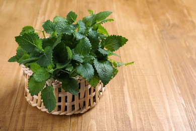 Photo of Fresh lemon balm in wicker basket on wooden table, space for text