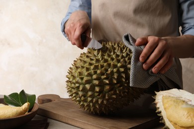 Photo of Woman cutting fresh ripe durian at table, closeup