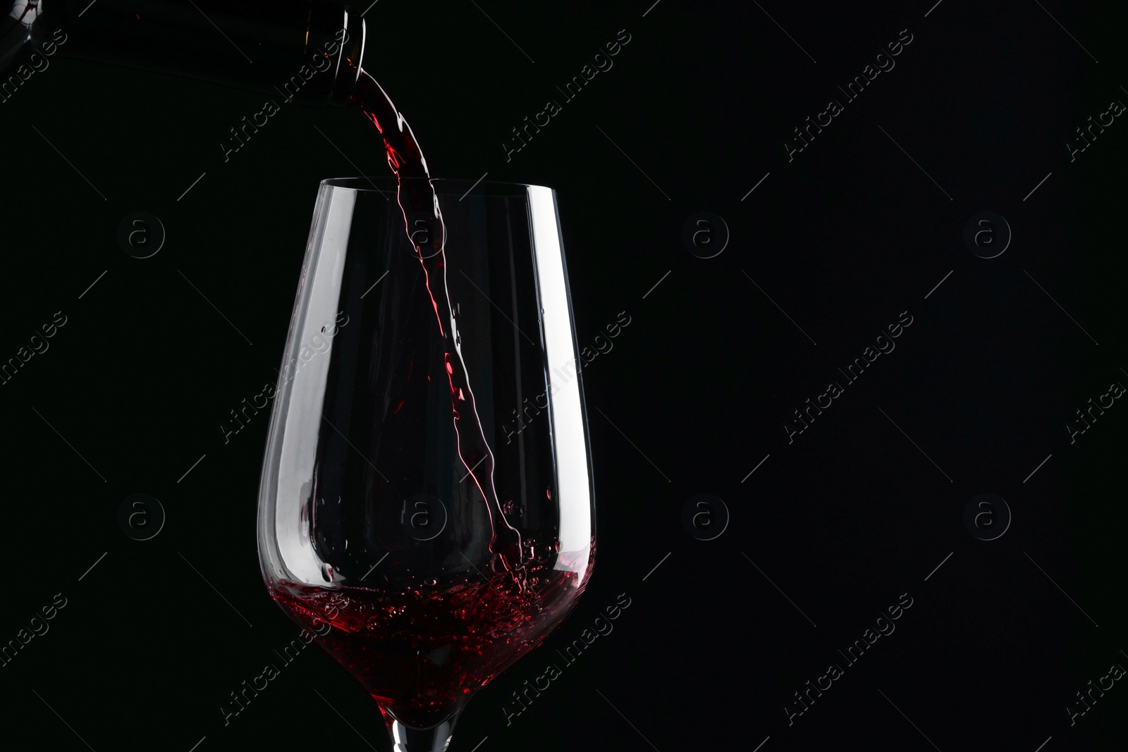 Photo of Pouring red wine into glass against black background, closeup. Space for text