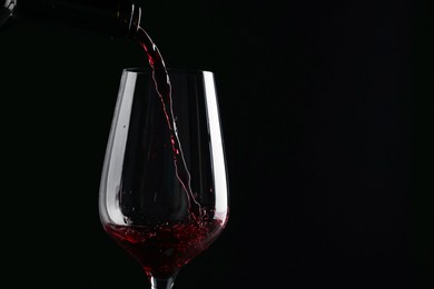 Photo of Pouring red wine into glass against black background, closeup. Space for text