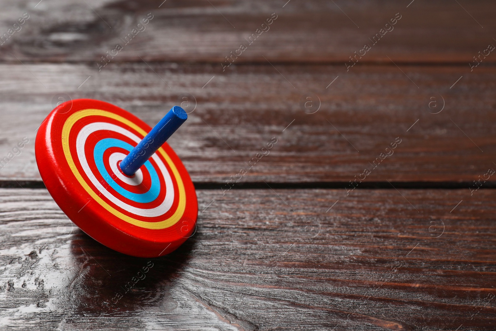 Photo of One bright spinning top on wooden table, closeup. Space for text