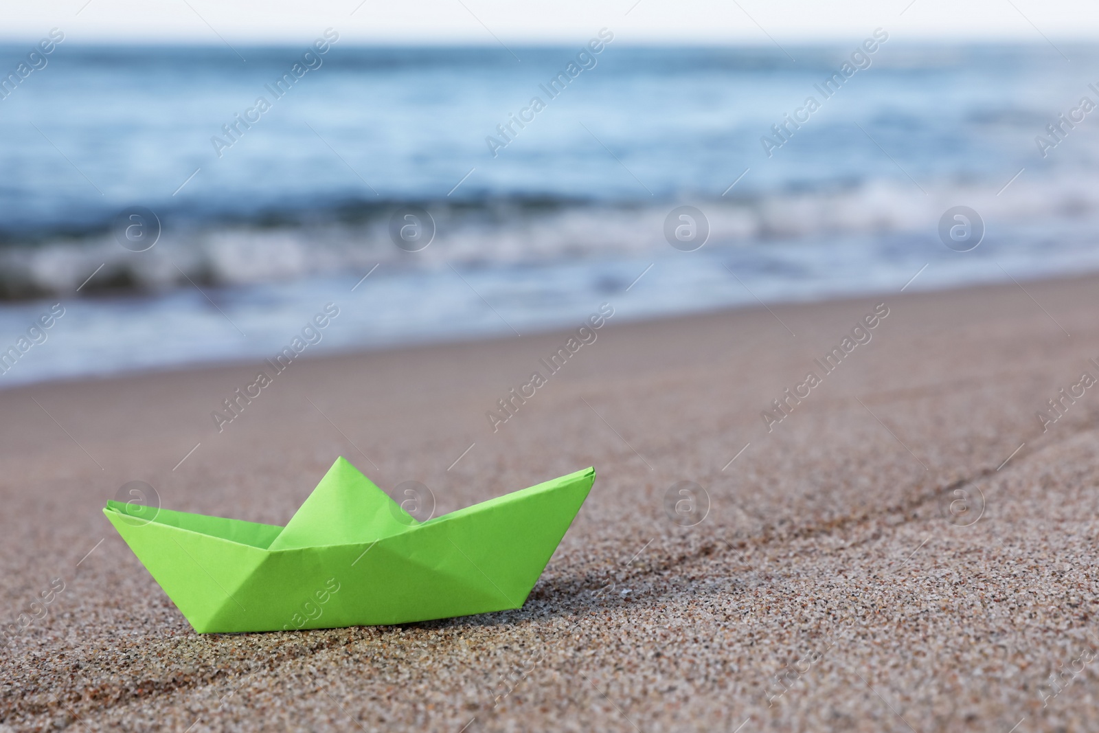 Photo of Light green paper boat near sea on sandy beach, space for text