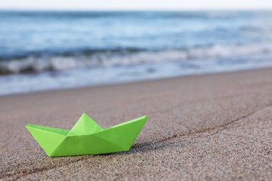 Light green paper boat near sea on sandy beach, space for text