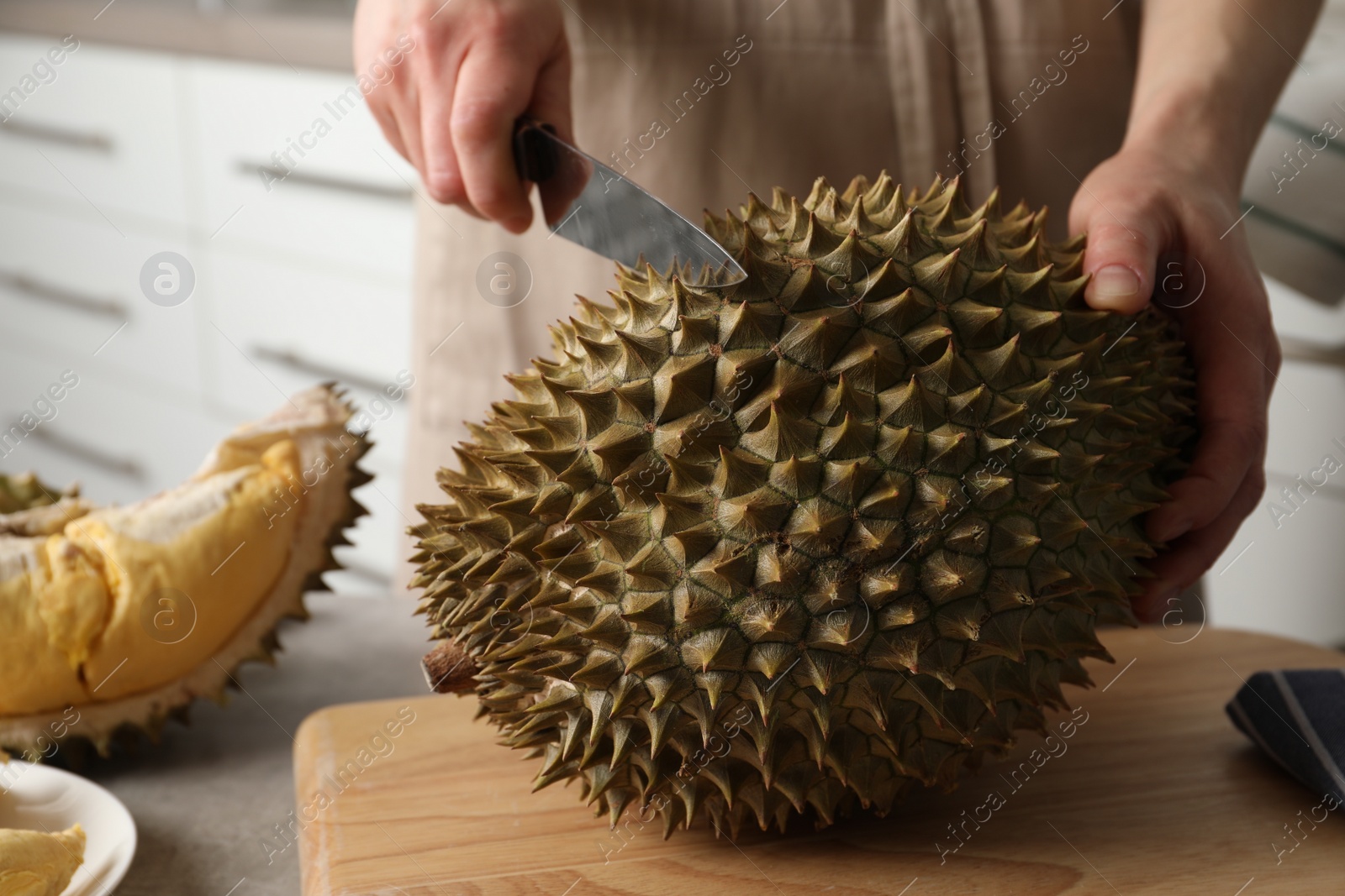 Photo of Woman cutting durian at table in kitchen, closeup