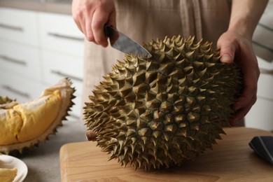 Photo of Woman cutting durian at table in kitchen, closeup